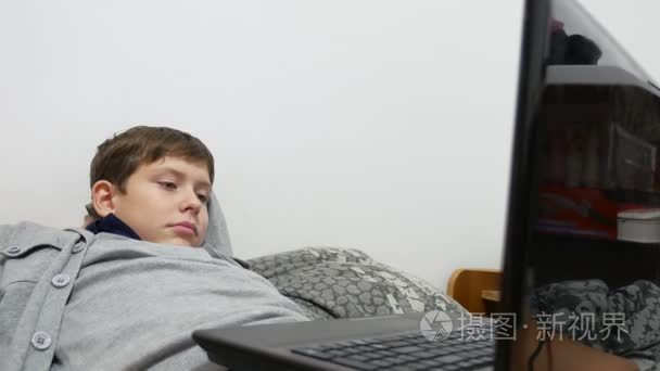 十几岁的男孩躺在床上在线的笔记本电脑上玩在线游戏
