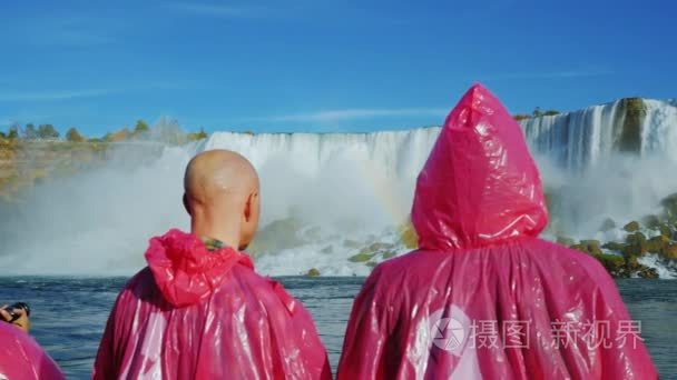 尼亚加拉大瀑布，纽约，美国2016年十月 20 查看从后面的两名游客在粉红色的雨衣。欣赏尼亚加拉大瀑布。站在板上一艘船，飞瀑视频