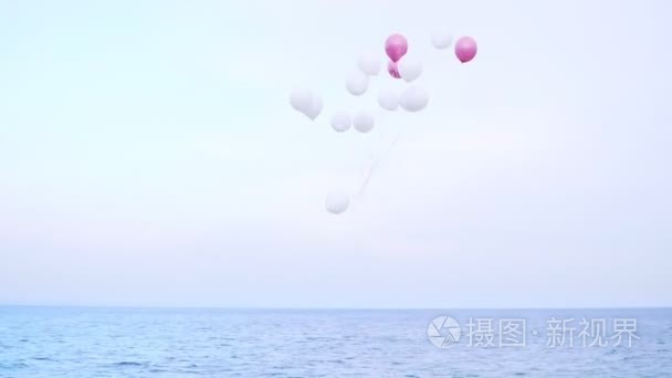 粉色和白色的气球飞在天空下的海