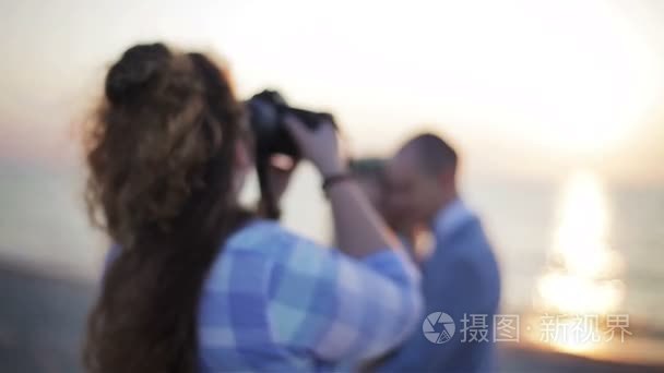 摄影师拍照不可识别夫妇在户外摆在海和背光太阳背景密切了浅景深。婚礼的婚礼和爱情故事摄影