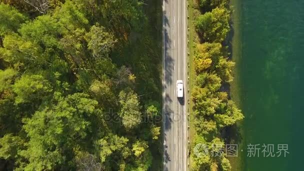 汽车在道路上骑湖附近的树木之间。绿色的森林。阳光灿烂的夏天春天的一天。绿色的水。山脉