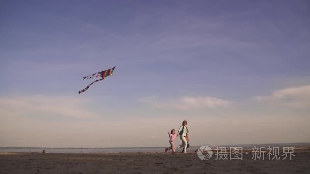 妈妈花时间与孩子们在户外在日落时分在海面上。家族在放风筝，快乐的春天。慢动作