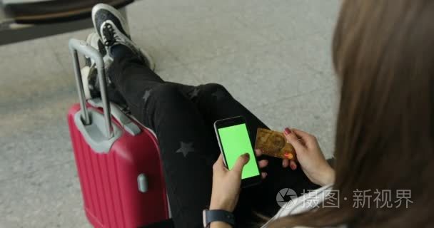 女孩使用智能手机与绿色屏幕。在线购物。美丽的年轻游客女孩与背包和携带行李在国际机场，等待她的航班，看起来神情沮丧视频