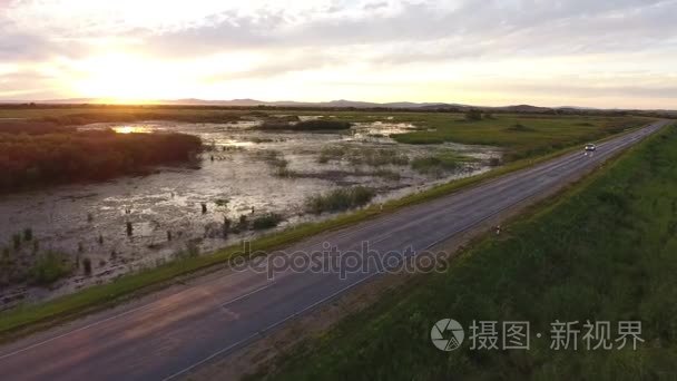 窄条笔直的道路跟着的车。美丽的七彩粉色和橙色落日的天空湖泊水中的倒影。俄罗斯滨海边疆区符拉迪沃斯托克 海参崴 性质。夏泉