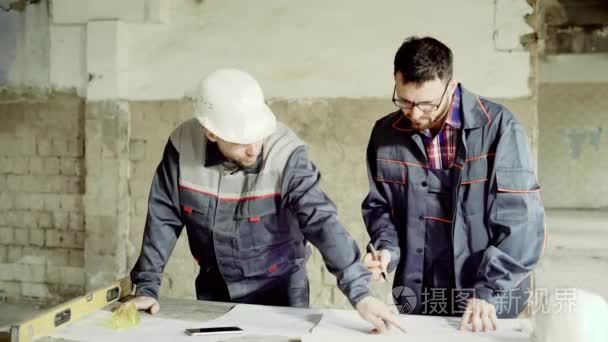 工程师和工头在防护头盔在施工图纸做笔记，男人是在一家工厂，将接受侦察结构