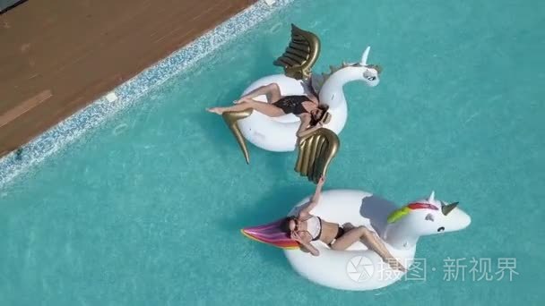 在空气床垫上晒日光浴，独角兽和飞马座的年轻女性。有吸引力的年轻女孩在游泳池休息在晴朗的一天。用直升机视频