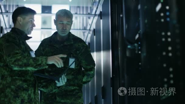 在数据中心两个军人一起打开服务器机架柜工作。一个拥有军事版笔记本电脑
