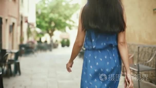 跟拍的女人在轻夏装的欧洲小镇的街道上走在阳光灿烂的日子视频