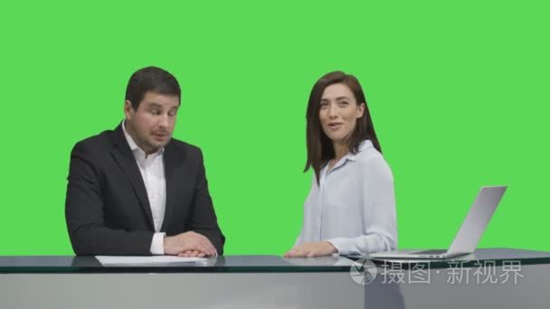男性和女性的广播都坐在一张桌子，说关于模拟绿色屏幕背景