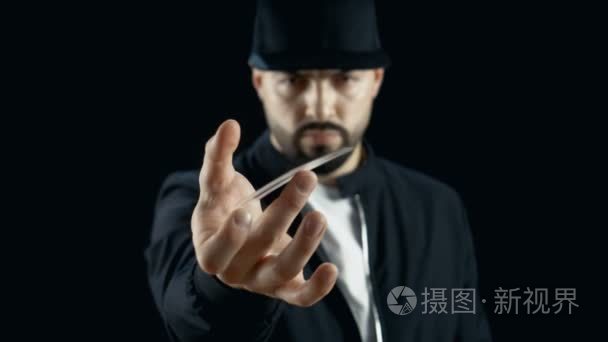 专业街头魔术师表演的花招纸牌戏法 纺一卡手指上的戴着帽子。背景是黑色
