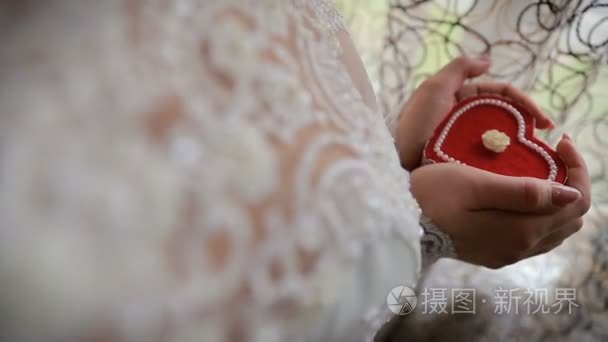美丽的女人手里拿着的心形状的订婚戒指盒子。拿着一个心形的礼品盒在她手中的新娘