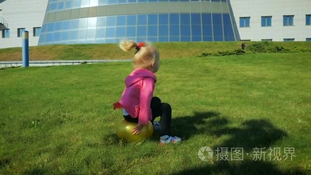 慢动作： 三岁的小女孩跳上一块草坪上的橡胶球