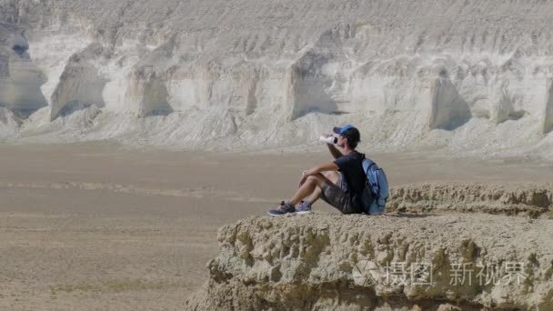 年轻的旅行者喝水在岩石上撞视频