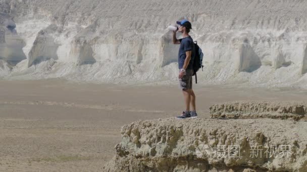 年轻的旅行者喝水在岩石上撞视频