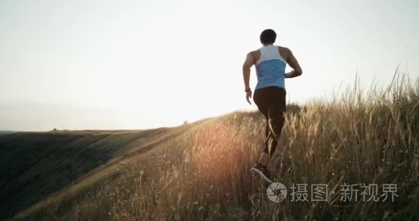 运行在日落时分慢跑的转轮男人。男慢跑训练马拉松跑运行上色彩斑斓的黄色天空衬托的山。适合健身模型生活健康活跃户外生活方式。4 k