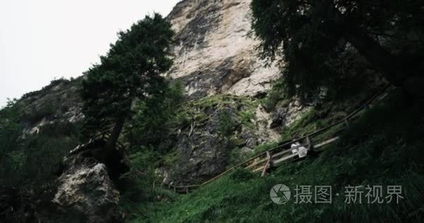 一对年轻的夫妇走下桥在森林与大山的背景。慢动作