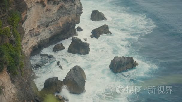 海浪冲破石崖。印度尼西亚巴厘岛热带海滩鸟瞰图。慢动作