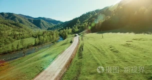 到 4k 的鸟瞰图。对山区农村土路和草甸在阳光灿烂的夏天早上低空中飞行。绿树 阳光和山区河流附近