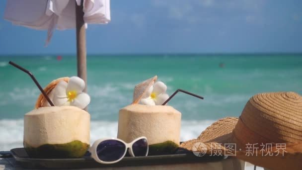 热带新鲜椰子鸡尾酒装饰的鸡蛋花, 帽子, 雨伞和太阳镜在海滩咖啡馆与变化的焦点, 以绿松石海背景。Slwo 的概念。1920x1
