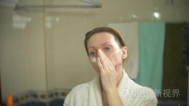 浴袍妇女在浴室里面和脖子上涂抹奶油。4k慢动作视频