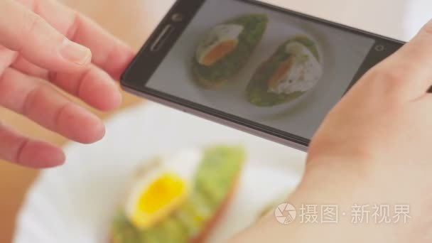 餐馆里的一个女人用手机相机拍了一张食物的照片。鸡蛋和鳄梨三明治视频