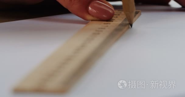 用铅笔和木制尺子在纸上画一条线的女性手。宏