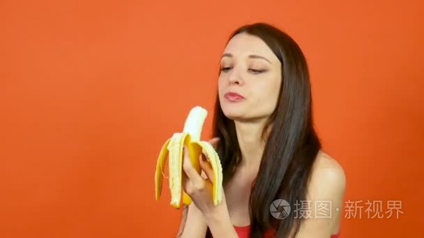 滑稽的年轻饥饿的妇女吃香蕉在明亮的橙色背景。热带水果。节食概念
