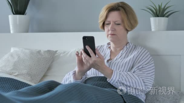 老妇人躺在床上使用智能手机视频