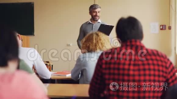 高中老师帅哥正在和坐在教室里的桌子旁微笑的学生交谈。 教育