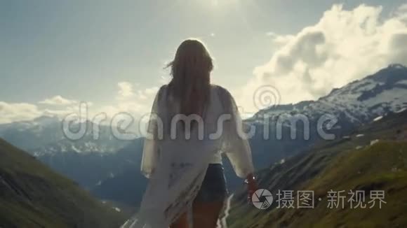 那个运动女孩站在阿尔卑斯山的山顶上。 她向太阳举手。
