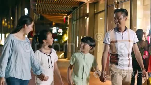 亚洲一家4口人，夜间慢动作在购物中心外散步和购物