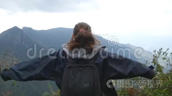 年轻的女徒步旅行者，背包伸向山顶，举起双手。 女游客站在