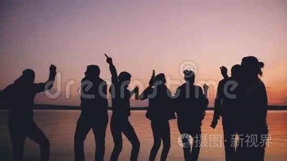 团体青年舞蹈家在日落时在海滩上举行派对