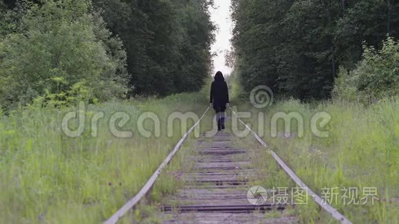 一个孤独的黑衣人走在树林里的铁轨上，后景。 他感到轻松、思考和无聊