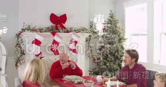 祖母带着圣诞火鸡给坐在餐桌旁的家人吃午餐。 父母帮助为孩子提供蔬菜