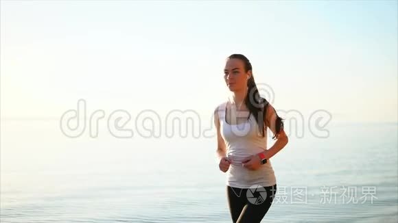 年轻漂亮的运动女人在海边跑步。