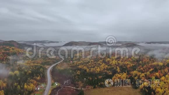 一架无人机在浓雾中在群山附近的一片秋色森林中从蜿蜒的道路上升起