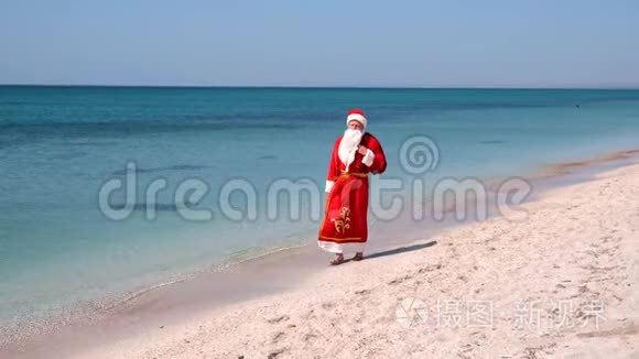 圣诞老人带着一袋礼物走在沙滩上。 青绿色的水。