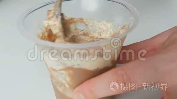 生奶油和巧克力在塑料杯中的甜点。 女性手用茶匙混合奶油的顶部