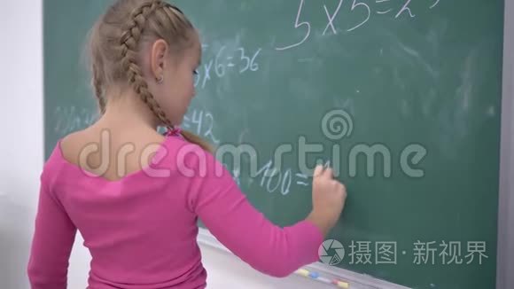 快乐的女学生用粉笔解决了学校绿色黑板上的数学例子，在课堂上，小学