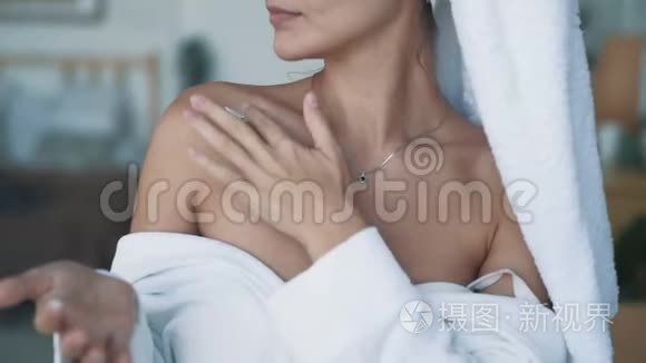 贴身穿浴袍的女人在肩膀上涂抹奶油，动作缓慢