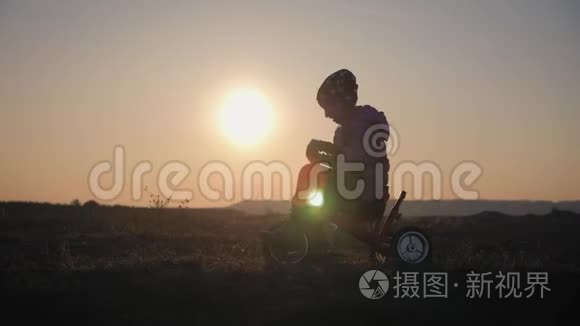 日落背景下骑自行车的女孩的剪影。孩子在夕阳下玩自行车。