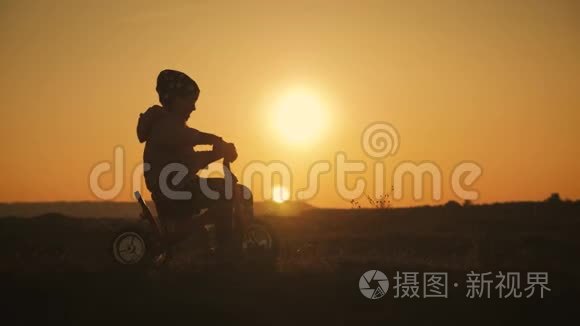 日落背景下骑自行车的女孩的剪影。孩子在夕阳下玩自行车。