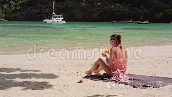 一个美丽的年轻女孩坐在海滩上，用防晒霜涂抹她的身体。