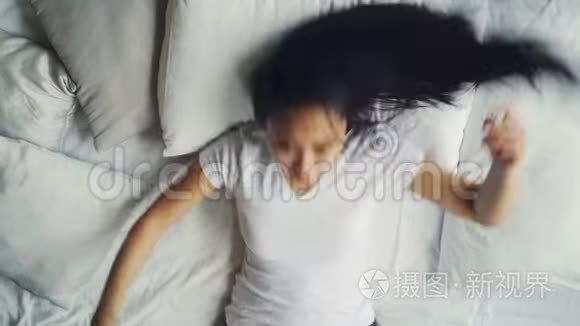 穿着休闲服装的亚洲女人躺在舒适的床上，铺着白色床单，抚摸着她的头发