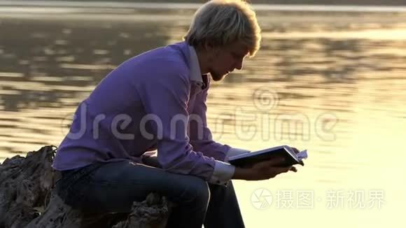学生坐在湖畔读一本手册视频