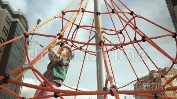 一个孩子在户外操场上爬上一根绳子的水平杆