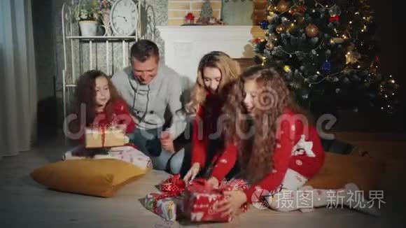 四个人的幸福家庭正在打开圣诞礼物。 新年之夜在圣诞树脚下