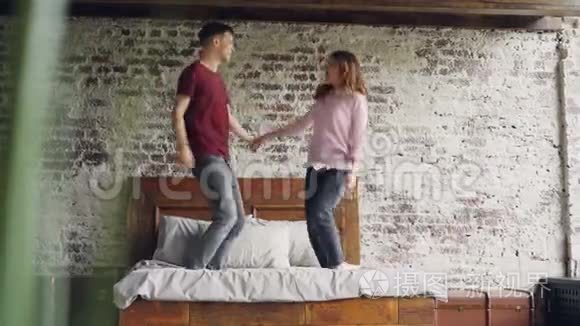 年轻的女朋友和男朋友正在双人床上跳舞，在卧室里亲吻在一起玩得开心。 快乐活跃的人