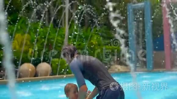 一位年轻的父亲和他的儿子在喷泉间的一个热带水池里玩得很开心